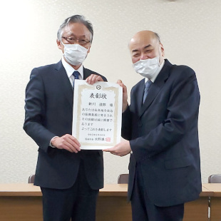 市功労者の表彰状を手に新川同志社大学院教授と記念撮影する水野市長