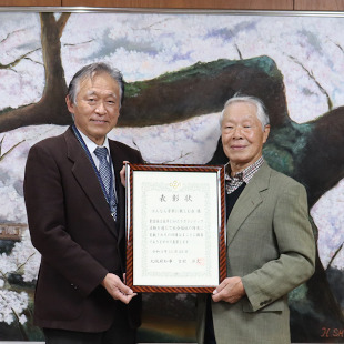 大阪府社会福祉ボランティア知事表彰の表彰状を手に、はんなん音楽に親しむ会の代表の林さんと記念撮影する水野市長