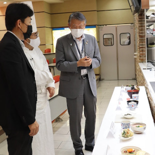 泉州美食EXPO・阪南市だし茶漬けレシピコンテストにて副校長からレシピ説明を受ける水野市長